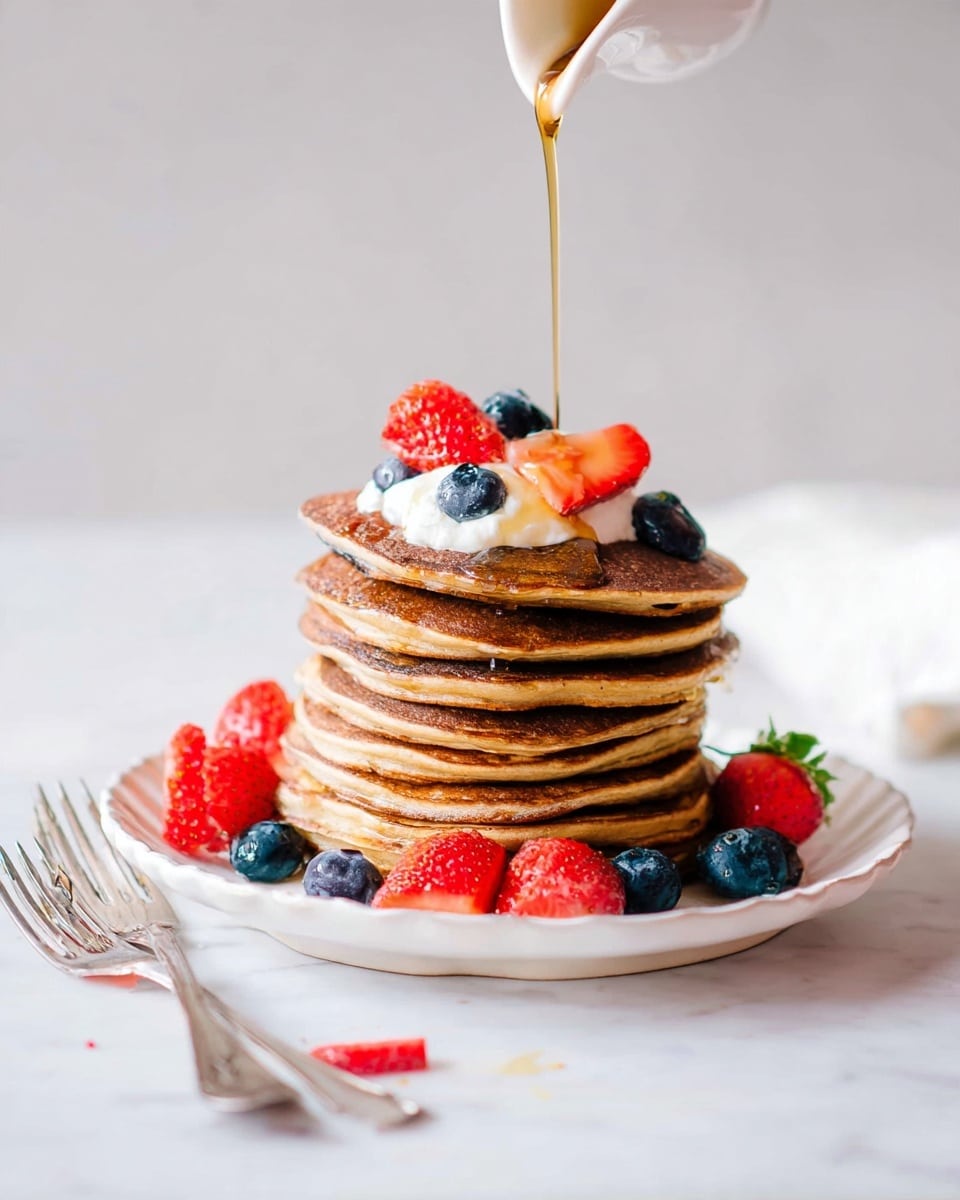 A tall stack of eight golden-brown pancakes sits on a white plate with a slightly scalloped edge. The pancakes look soft and fluffy, with even, round edges. On top, there is a dollop of white cream, surrounded by a few bright red strawberry pieces and plump blue blueberries. More strawberries and blueberries are scattered around the base of the stack on the plate. A woman's hand pours amber syrup from above, which flows over the top pancake and down the sides. Two silver forks rest on the left side of the plate, one with a bit of fruit on it. The scene is set on a white marbled surface with soft, bright lighting. Photo taken with an iphone --ar 4:5 --v 7
