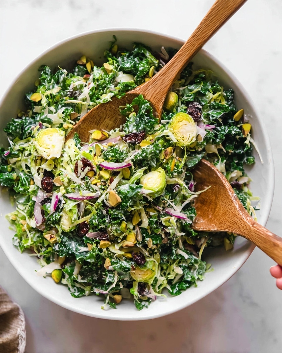 A bright green salad in a white bowl is filled with finely chopped kale and shaved Brussels sprouts as the base layer. Thin slices of purple onion and small pieces of green celery are scattered throughout, adding contrast. There are also yellowish-white shaved parmesan cheese curls and small brownish-green pistachio nuts mixed in. The salad is lightly coated with a creamy dressing, giving it a slightly glossy look. Two wooden salad spoons rest on top, one of them being held by a woman's hand. The bowl sits on a white marbled surface. photo taken with an iphone --ar 4:5 --v 7