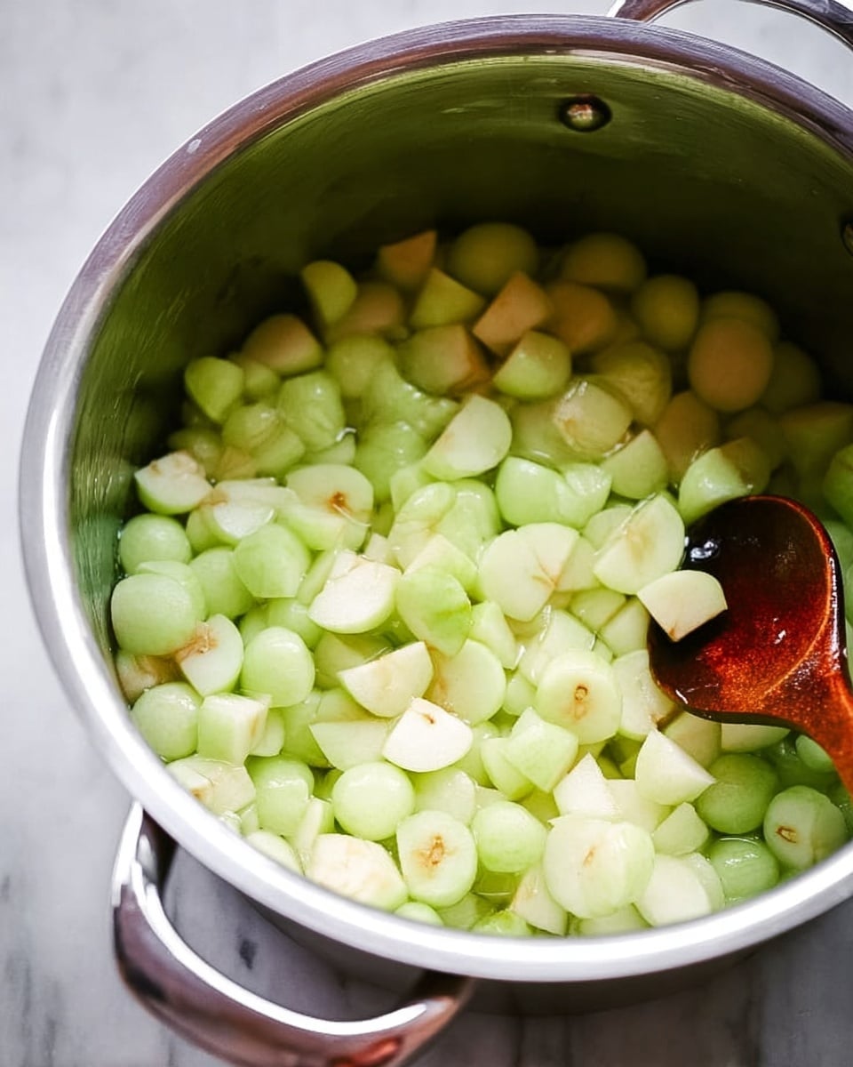 A shiny silver pot filled with many small, light green and white apple pieces, with a few light brown spots on their edges. The pieces fill about three-quarters of the pot. A wooden spoon rests inside the pot on the right side, its dark brown color contrasting with the light apples. The pot sits on a white marbled surface. photo taken with an iphone --ar 4:5 --v 7