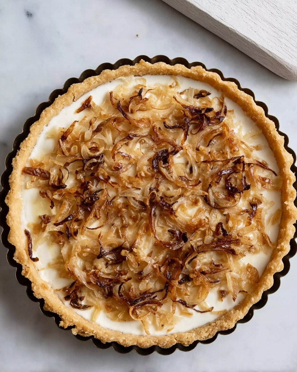 A round tart with a golden-baked crust forming a raised edge is shown from above. Inside the crust, there is a smooth, creamy white layer forming the base of the tart. On top of this base, there are thinly sliced cooked onions scattered evenly, with colors ranging from light golden brown to dark caramelized brown, adding a textured look. The tart is placed on a white marbled surface, and a white wooden board is partly visible at the top right corner of the image. photo taken with an iphone --ar 4:5 --v 7