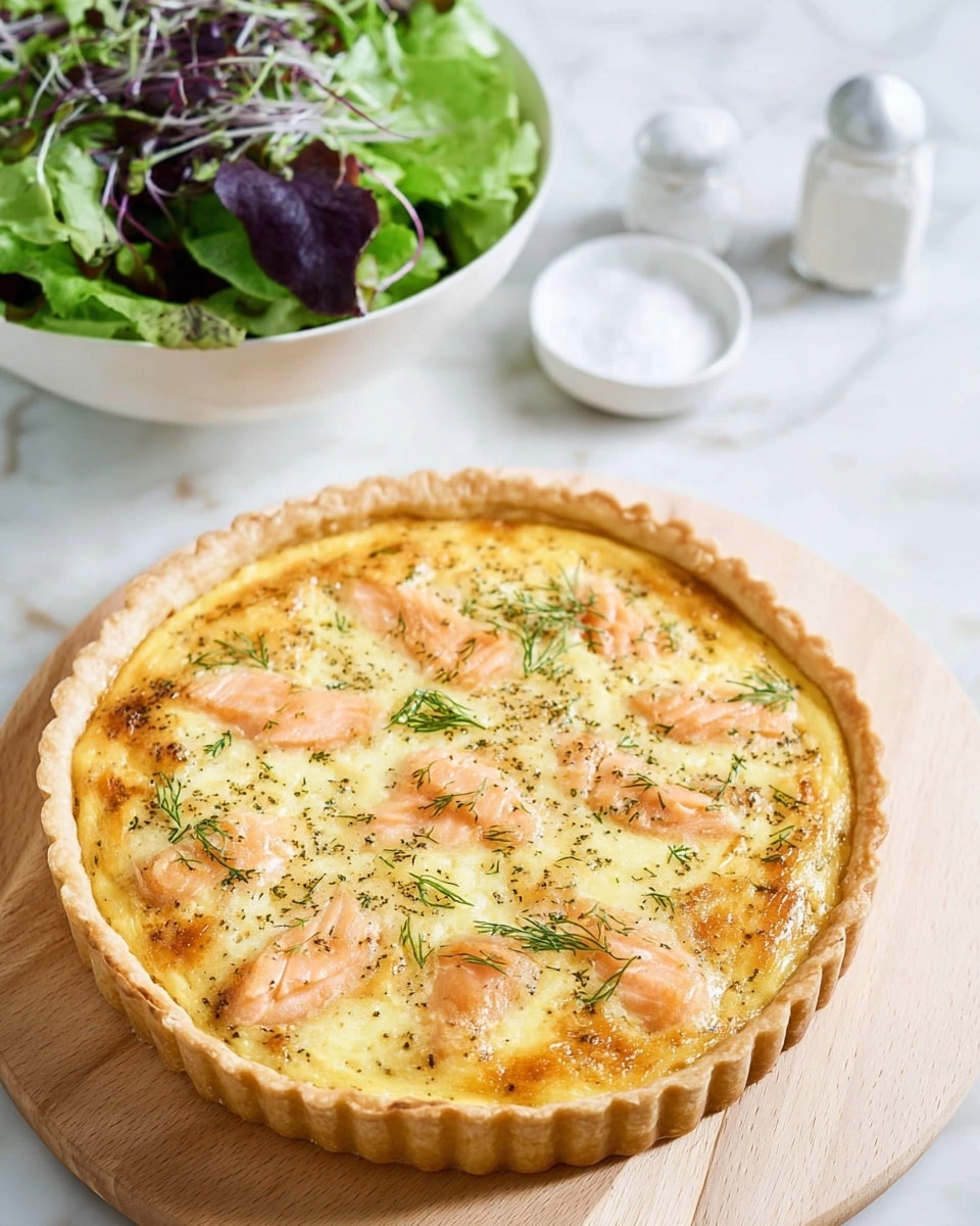 A round quiche with a golden brown crust sits on a light wooden board, showing a creamy yellow egg filling layered with light pink smoked salmon pieces scattered evenly on top, sprinkled with small green dill leaves. The quiche crust has a slightly scalloped edge and a smooth texture. In the background, there is a white bowl of green mixed salad leaves with thin purple sprouts sitting on a white marbled surface, accompanied by a small white dish filled with coarse salt and a white pepper shaker nearby. photo taken with an iphone --ar 4:5 --v 7